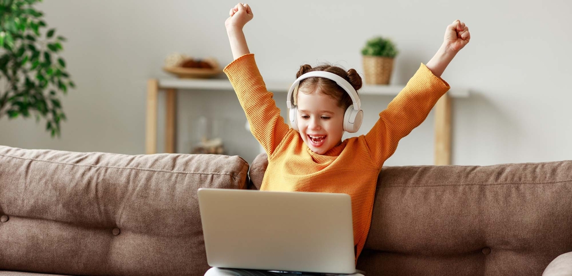 ein Mädchen sitzt mit Kopfhörern vor dem Laptop und freut sich über ein gewonnenes Spiel