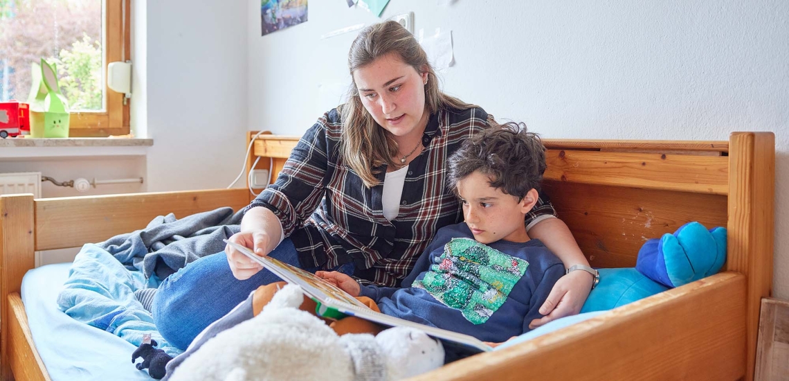 Eine Erzieherin liest einem Jungen ein Buch vor.