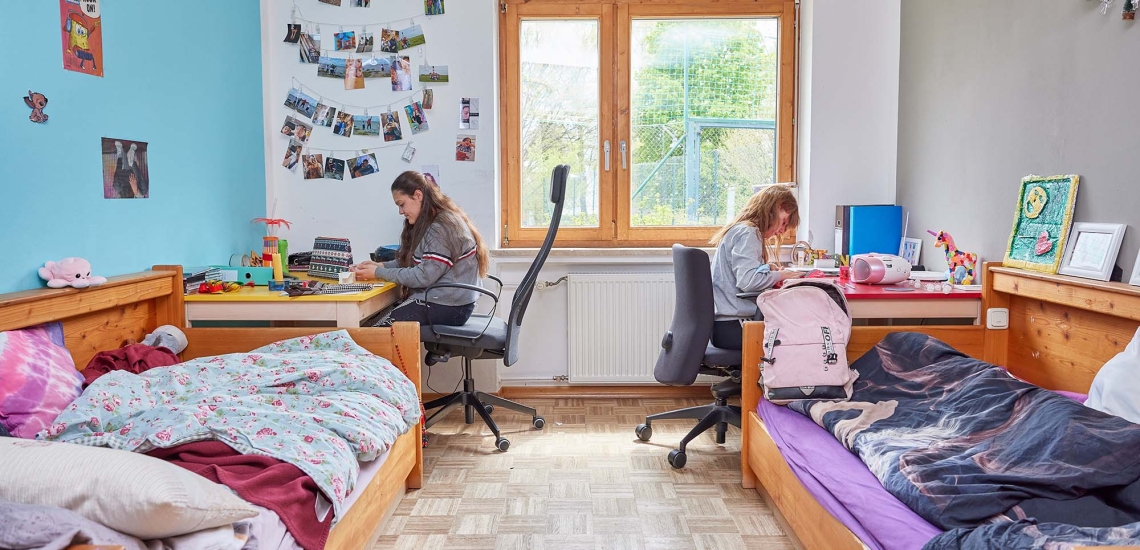 Zwei Mädchen sitzen in ihrem Zimmer an ihren Schreibtischen.