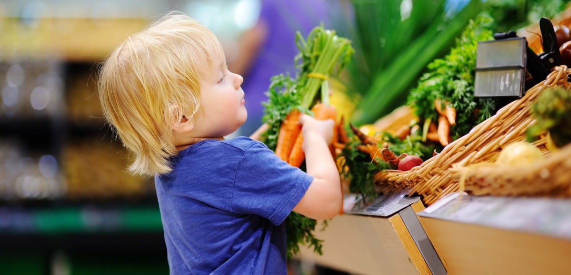 Ein kleiner Junge holt ein Bund Möhren vom Gemüsestand.