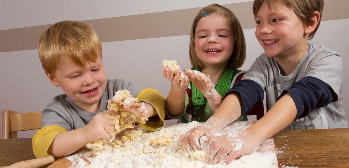 Drei Kinder beim Plätzchenbacken mit Teig an den Händen um im Gesicht 