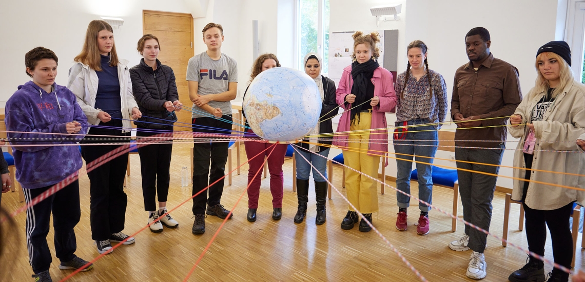 Junge Freiwillige balancieren auf Fäden eine aufblasbare Weltkugel.