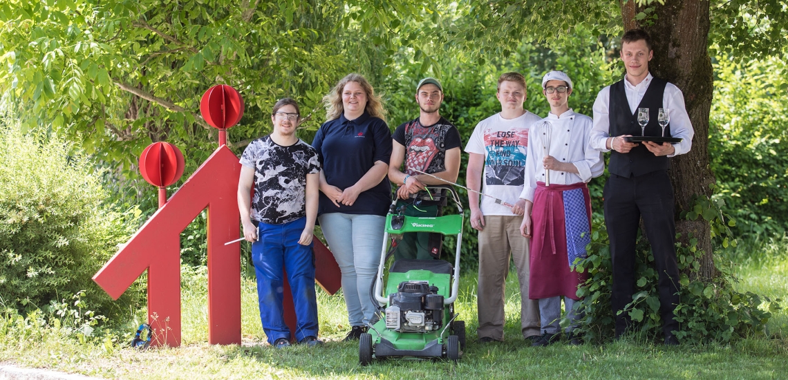 Eine Gruppe Jugendlicher steht auf der Wiese neben einem großen Don Bosco Logo.