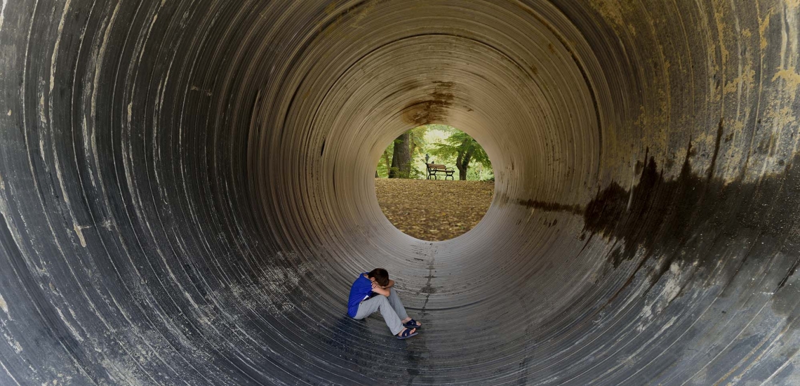 Ein Kind sitzt zusammengekauert in einem Tunnel und versteckt den Kopf in seinen Armen.