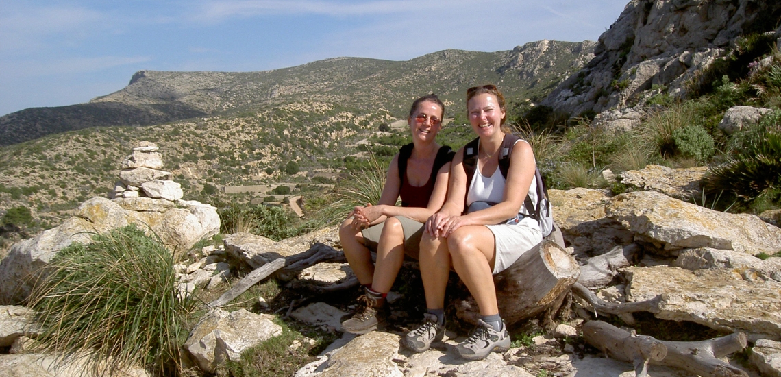 Angelika und Heike machen eine Wanderpause und sitzen nebeneinander auf Steinen.