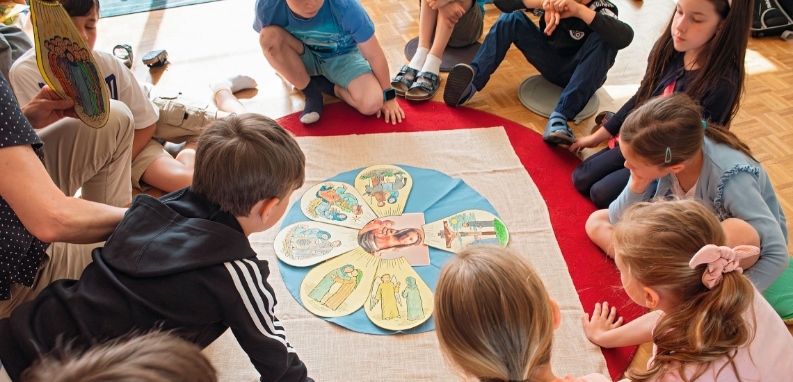 Kinder sitzen in Kreis auf Boden und beugen sich über Blüte aus Papierbildern