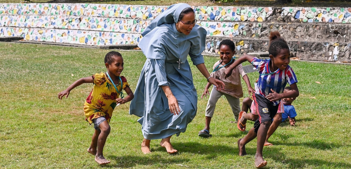 Don Bosco Schwester rennt beim Spielen mit Kindern über eine Wiese 