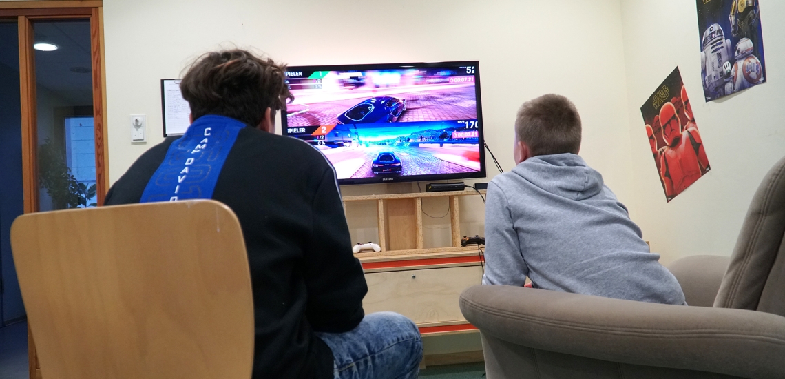 Zwei Jungs sitzen vor einem Bildschirm und treten bei einem Autorennen gegeneinander an.