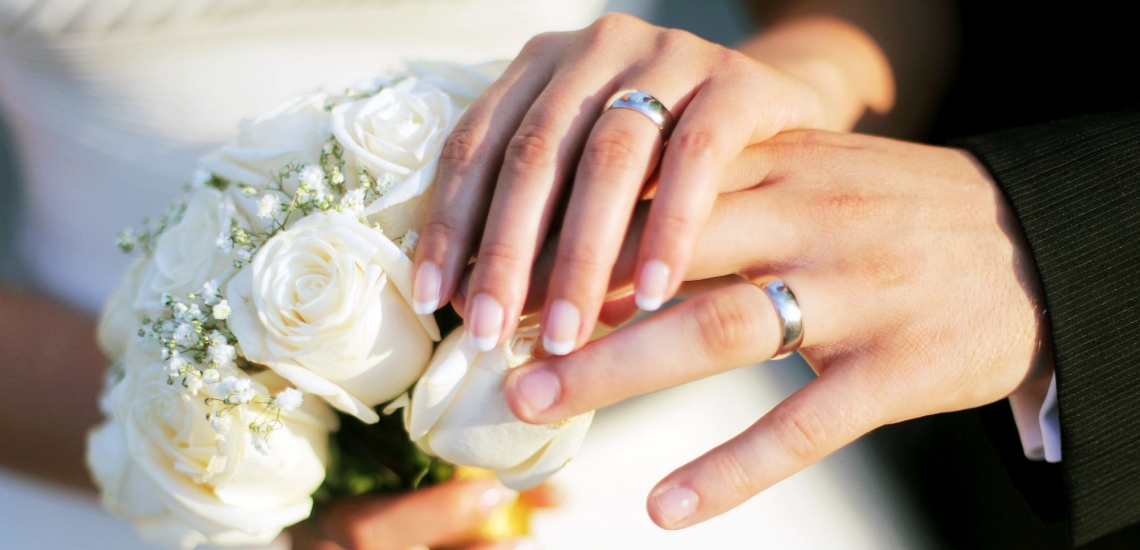 Hände von Brautpaar mit Eheringen und Brautstrauß 