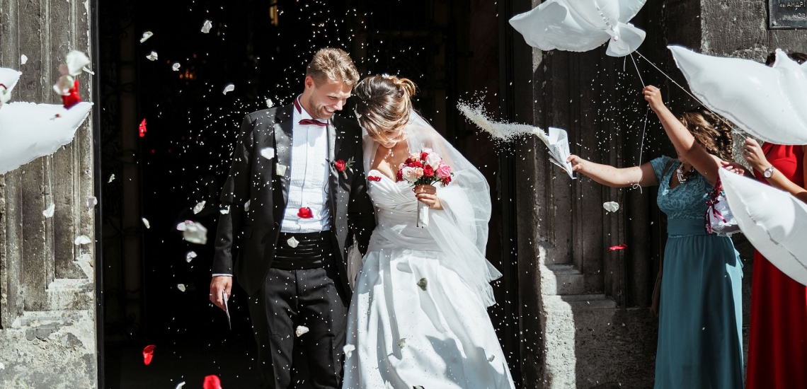 Hochzeitspaar wrid nach Trauung vor der Kirchentür von Gästen gefeiert mit Blüten und Ballons 
