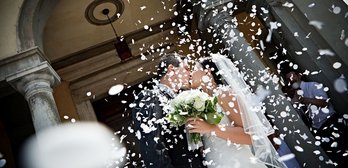 Hochzeitspaar küsst sich vor Kirche in Regen aus weißen Konfetti 