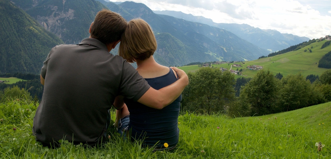 Junges Paar liebevoll aneinander angelehnt schaut auf Bergpanorama 
