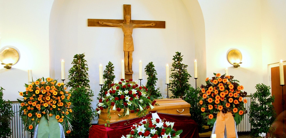 Mit Blumen geschmückter Sarg in einer Trauerhalle mit großem Kreuz 