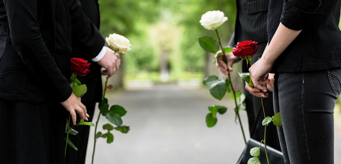 Schwarz gekleidete Trauernde mit weißen und roten Rosen auf dem Friedhof