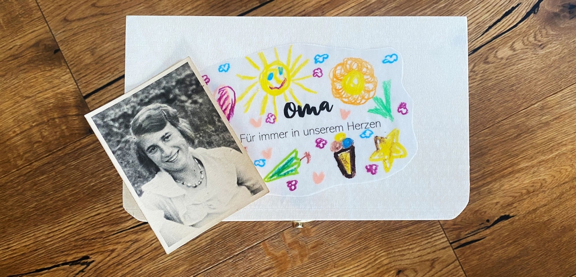 Mit bunten Farben bemalte Holzbox mit Schrift "Oma, für immer in unserem Herzen" und Foto der Oma als junge Frau