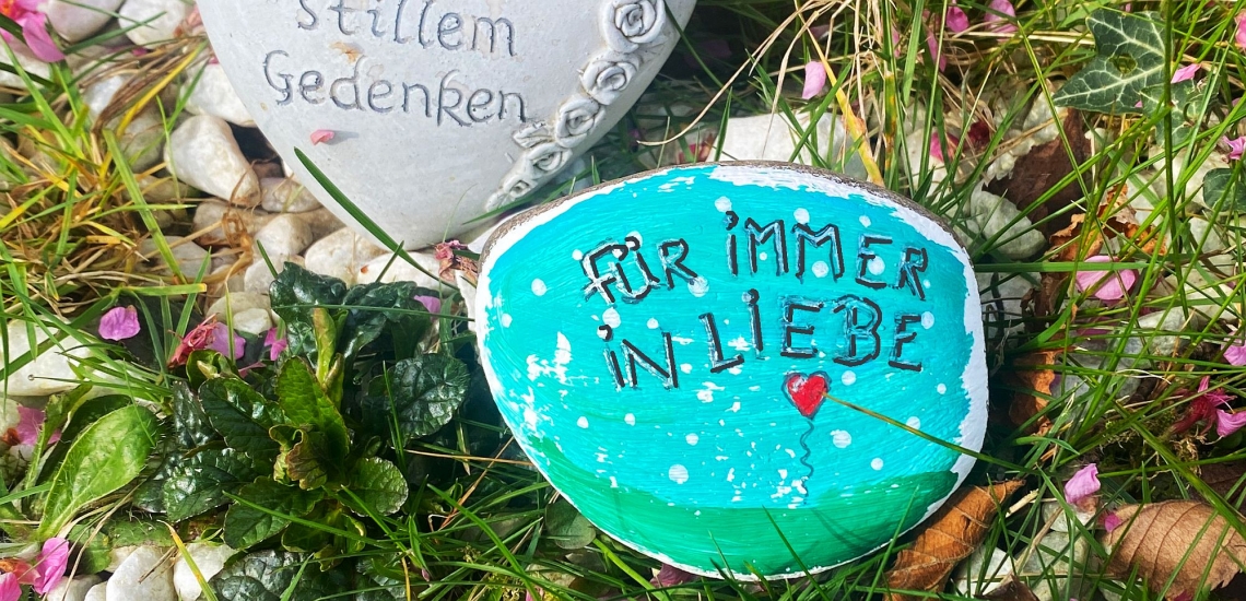 Mit bunten Farben bemalter Stein mit Schrift "Für immer in Liebe" auf einem Grab 