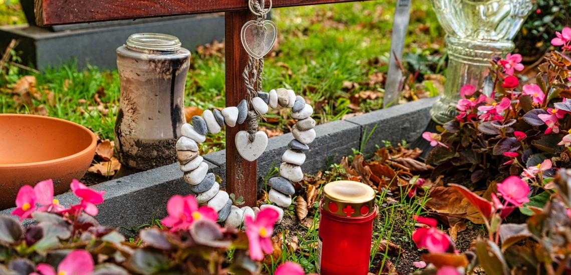 Grab mit Holzkreuz, Blumen, Herz aus Steinen und Kerze 
