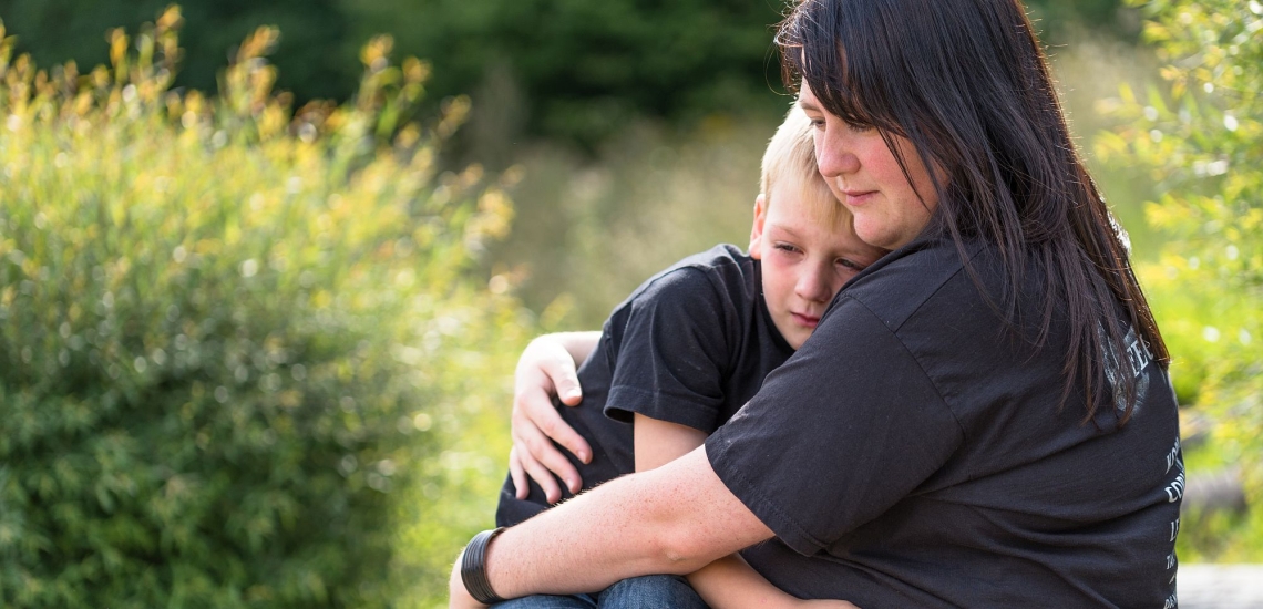 Mutter und Kind sitzen umarmt im Grünen und sind traurig 