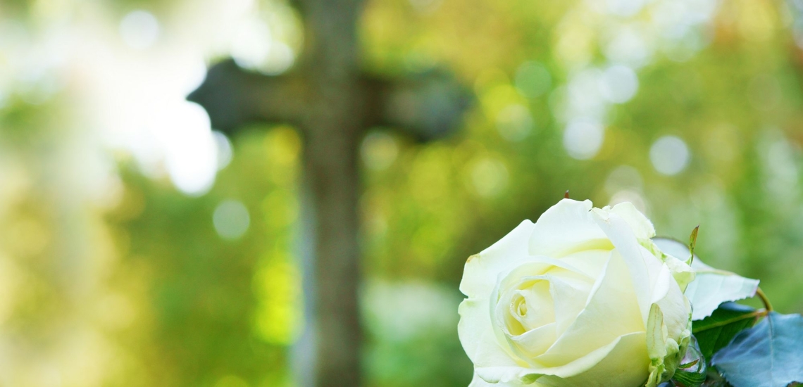 Steinkreuz und weiße Rose auf einem Friedhof 