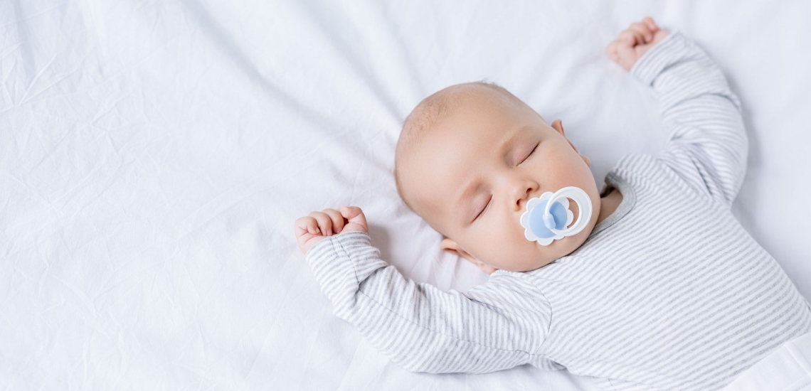 Baby im Strampelanzug mit Schnuller im Mund schlafend im Bett 
