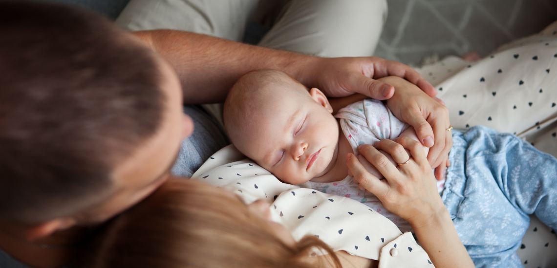 Eltern in Umarmung auf dem Sofa halten neugeborenes Baby 