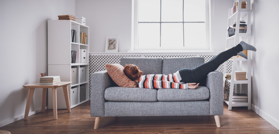 Frau liegt völlig erschöpft auf dem Sofa auf dem Bauch 