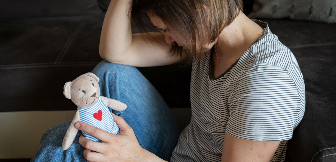 Frau trauert mit Stofftier in der Hand