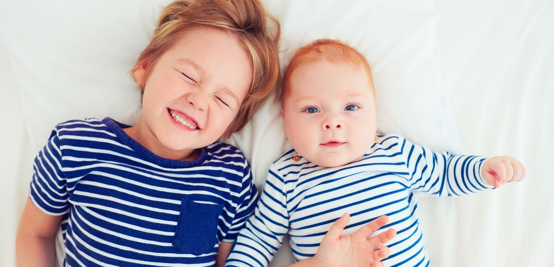 Großer Bruder liegt fröhlich mit Babybruder auf dem Bett 