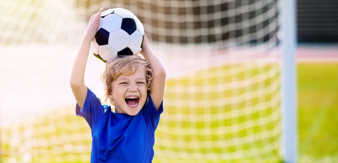 Junge auf Fußballplatz hält stolz einen Fußball in die Luft