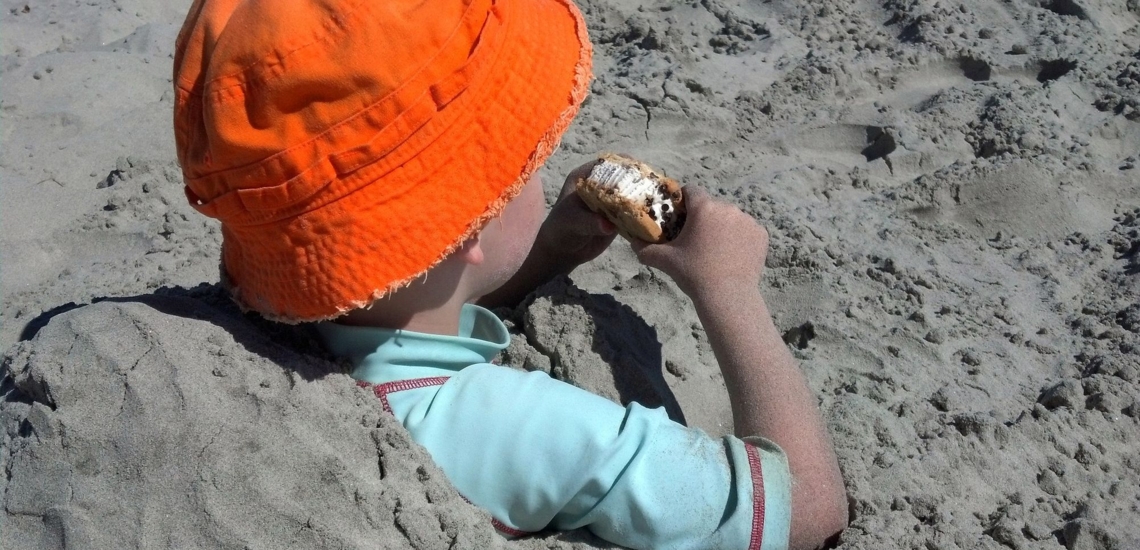 Junge sitzt eingebuddelt im Sand und isst