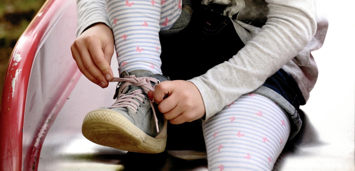 Kind sitzt auf Rutsche und bindet Schleife am Schuh 