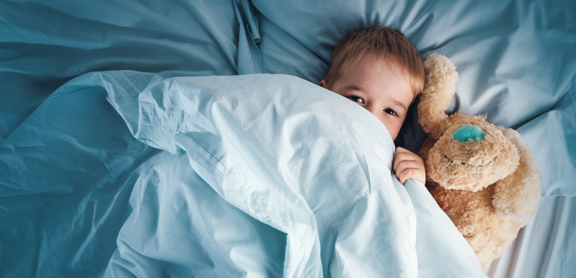 Kleinkind mit Teddy liegt im Bett und hat die Augen offen