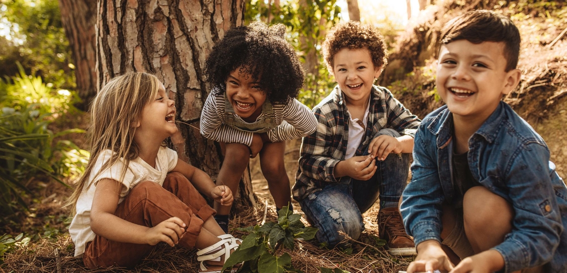 Kinder sitzen lachend auf Waldboden und spielen 