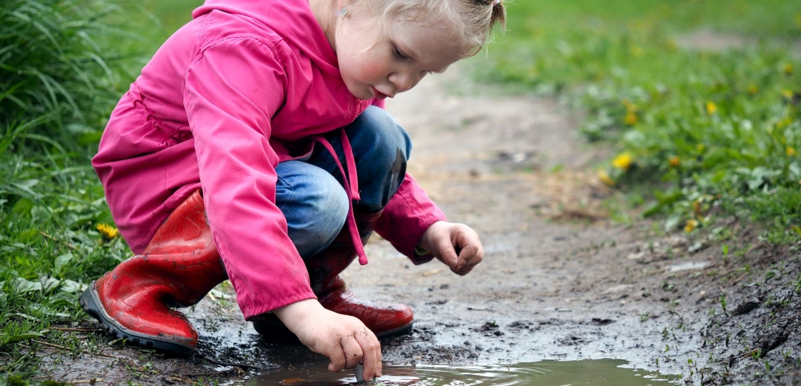 Mädchen in Regenkleidung spielt in Pfütze 