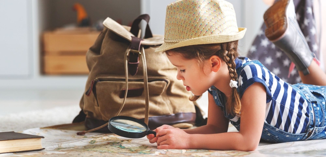 Mädchen mit Rucksack, Lupe und Landkarte spielt daheim Urlaub 