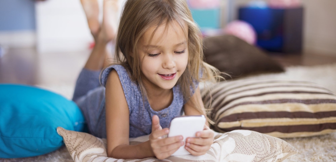 Mädchen liegt auf dem Boden und schaut ins Smartphone 