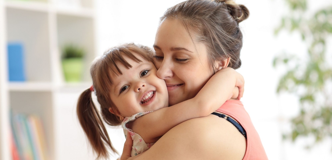 Mutter und kleine Tochter umarmen sich liebevoll und lächeln glücklich 