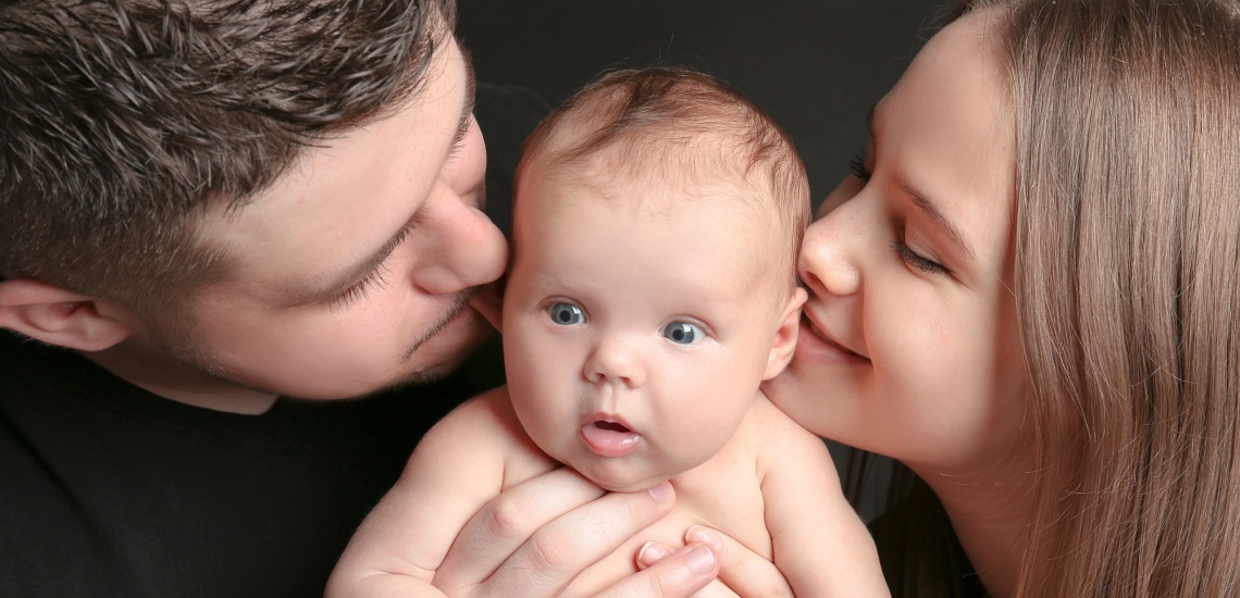 Vater und Mutter küssen Baby, Baby guckt erstaunt 