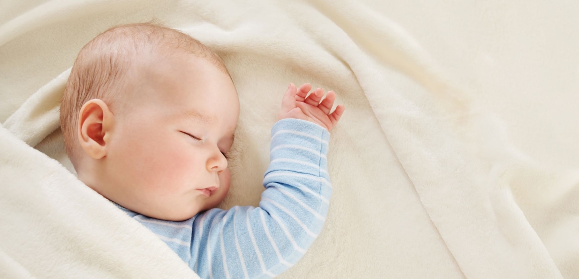 Säugling in hellblauem Strampelanzug schläft ruhig in einem Bett 