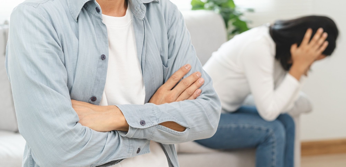 Paar sitzt schweigend und voneinander abgewandt nach Streit auf Couch im Wohnzimmer 