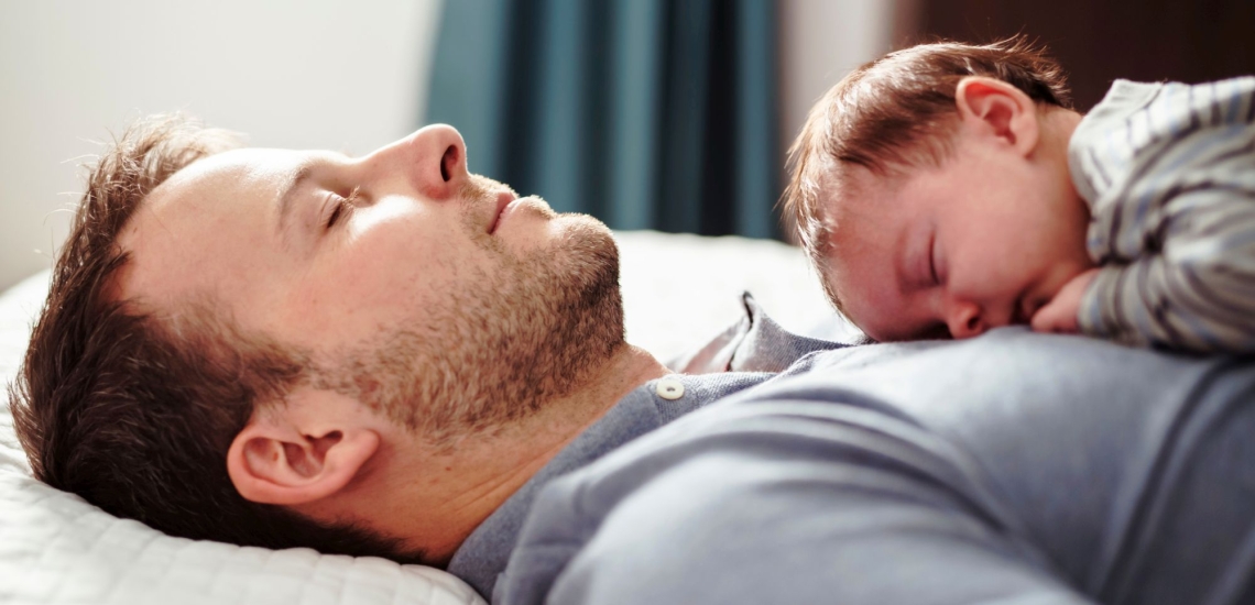 Baby schläft auf Bauch des Vaters in Bett 