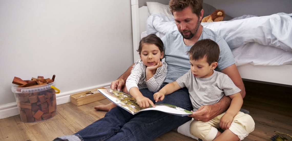 Vater und zwei Kinder schauen Bilderbuch an 