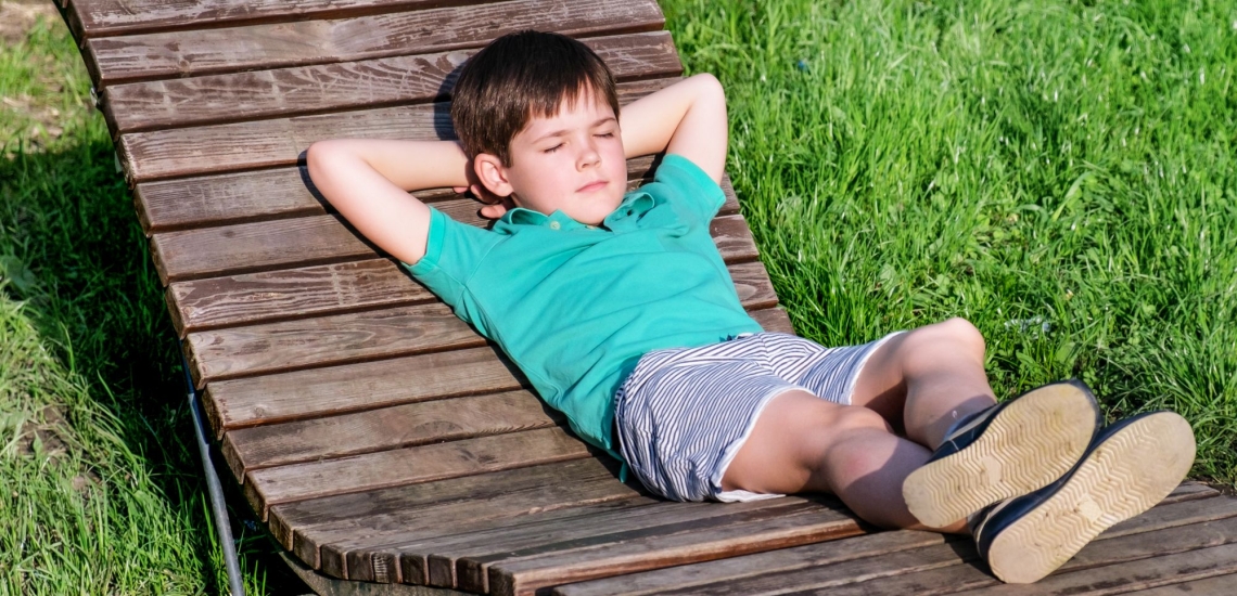 Junge ruht mit geschlossenen Augen auf einer Holzliege auf einer Wiese 