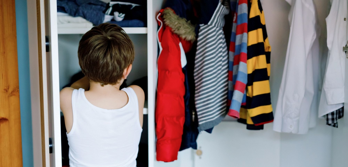 Kind steht vor Kleiderschrank und sucht Kleidung aus 