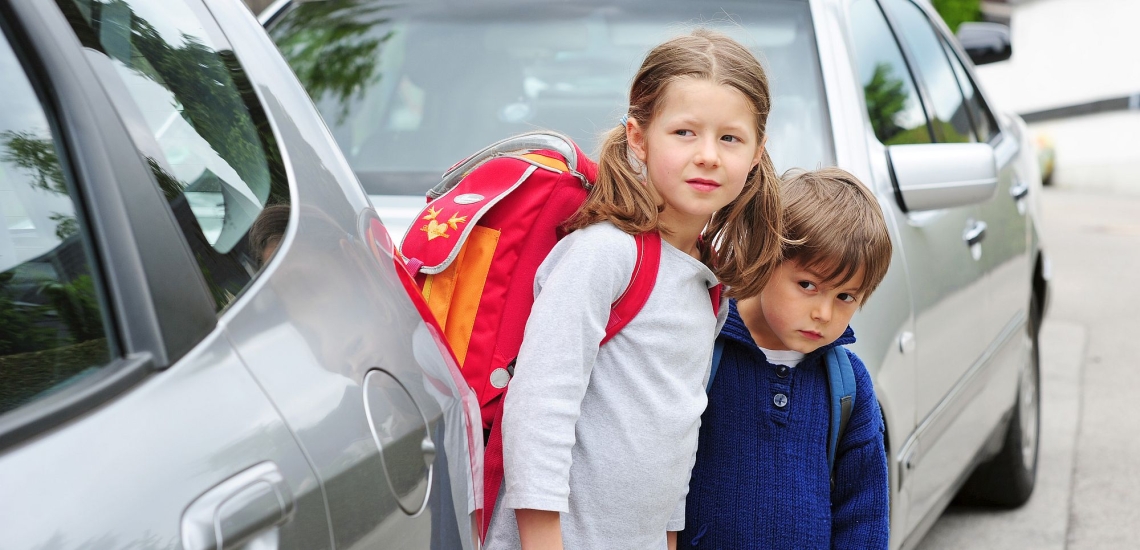 zwei Kinder zwischen Autos wollen die Straße überqueren 