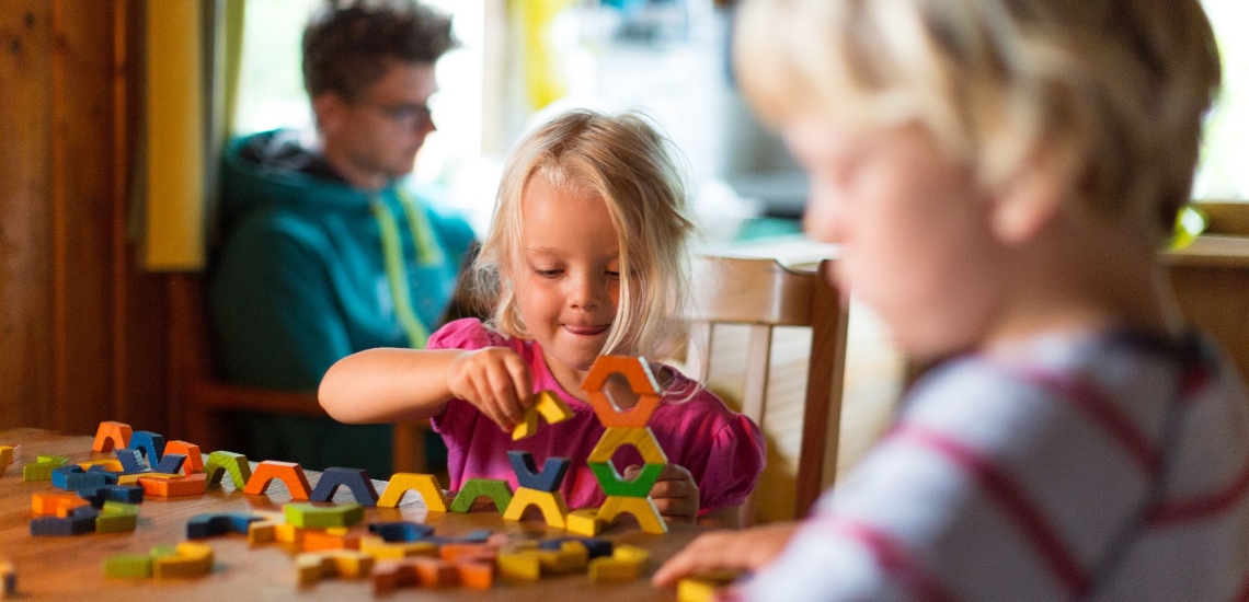 Kinder spielen mit Bauklötzen, Vater sitzt im Hintergrund 