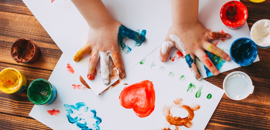 Kreative Kinderhände mit Fingerfaben und Papier mit bunten Bildern 