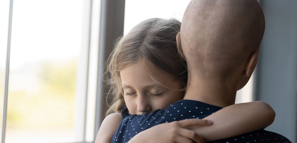 Mädchen umarmt innig seine Mutter, die Krebs hat und deren Kopf kahlgeschoren ist 