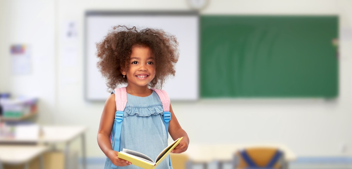 Mädchen glücklich mit Rucksack und Buch in Klassenzimmer