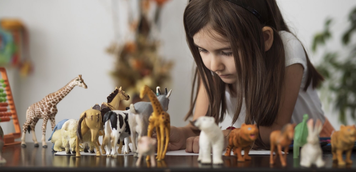Mädchen spielt versunken mit Tierfiguren, die auf Tisch aufgereiht sind 